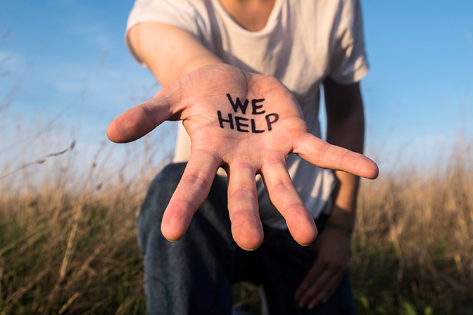 A person on their knee in a field with hand out and the words we help written on their hand