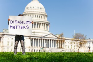 A person stands in front of a capital building holding a sign that says disability matters
