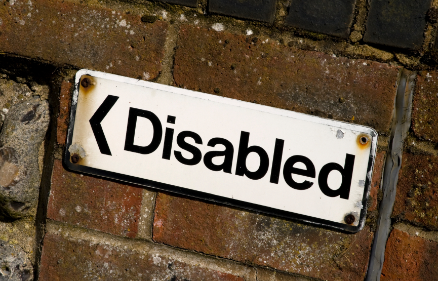 A brick wall has a sign that points to the left and says "disabled"