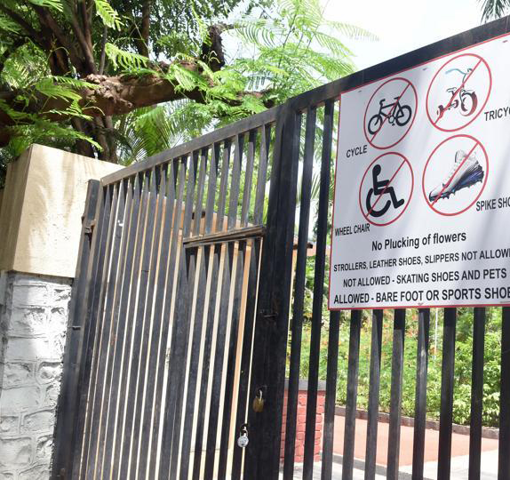 A metal gate has a sign with symbols that indicate no bicycles, no tricycles, no spiked shoes, no wheelchairs, no plucking of flowers